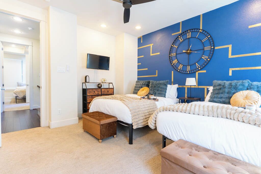 Een slaapkamer met twee bedden, een grote wandklok, een televisie en een dressoir.