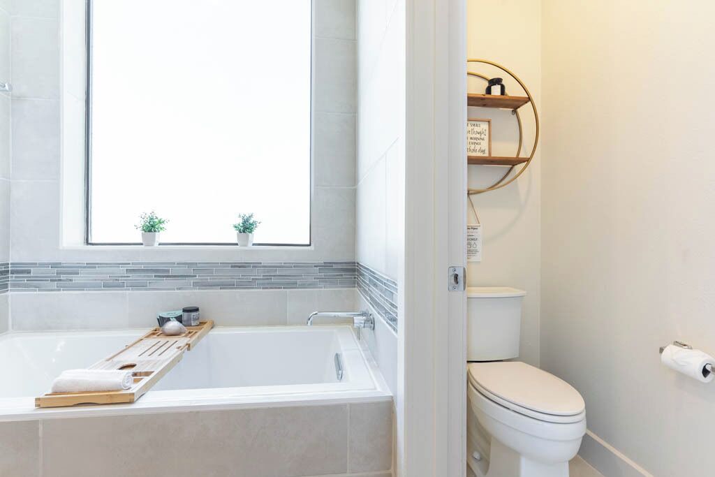 A modern bathroom with a bathtub, a toilet, and a window with two small potted plants.