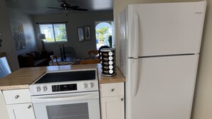 Una cocina con un refrigerador blanco, una estufa y un lavamanos. Hay botellas sobre la encimera.