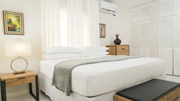 Une chambre bien rangée, avec un lit, des tables de chevet, un banc et une armoire.