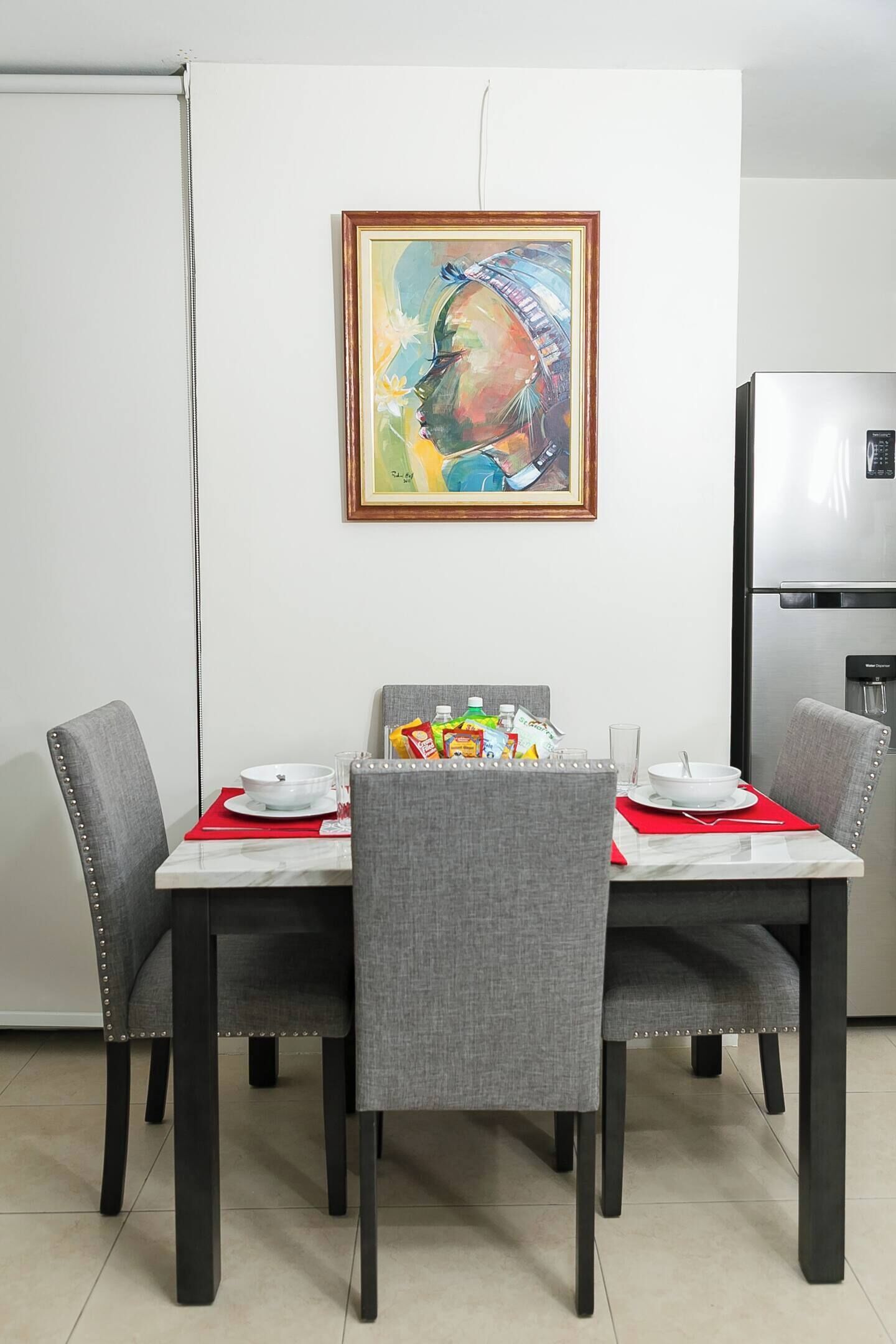 Ein Essbereich mit einem Tisch für vier Personen, grau gepolsterten Stühlen, einem Bild an der Wand und einem Edelstahl-Kühlschrank.