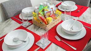 Une table à manger est dressée avec de l’assiette blanche, des couverts en argent et des sets de table rouges. Un panier de collations est placé au centre.