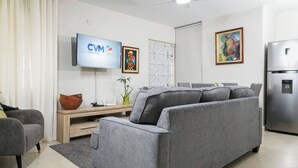 Un salon moderne avec un canapé gris, un téléviseur fixé au mur et un réfrigérateur.