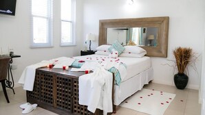 Quarto com cama, mesa de cabeceira, espelho e planta em vaso.