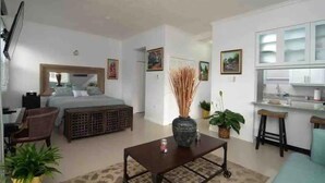 Quarto de hotel moderno com cama, escrivaninha, cadeira, mesinha de centro e cozinha.