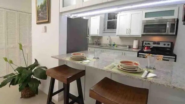 Cozinha com armários brancos, forno de aço inoxidável e bancada de mármore.