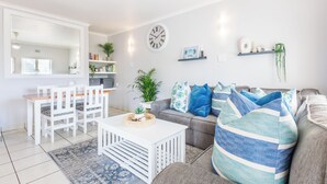 Una sala de estar moderna con comedor, que incluye un sofá, sillas, una mesa de centro y un reloj en la pared.