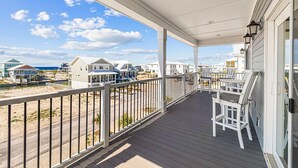 A covered porch with a view of beach houses and the ocean. - Serendipity Cottage (Navarre)