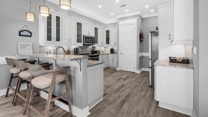 A modern kitchen with white cabinets, a central island with bar stools, and pendant lighting. - Serendipity Cottage (Navarre)