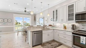 A modern kitchen with white cabinets, stainless steel appliances, and a large island. - Serendipity Cottage (Navarre)
