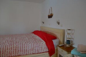 A bedroom with a bed, a bedside table, a nightstand, a lamp, and a wall-mounted shelf. - The Red-Fish House - 1 (Astipalea)