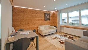 A modern living room with a wooden wall, a white sofa, a dining table with chairs, and a cowhide rug. - Studio Aosta (Zermatt)