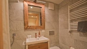 A bathroom with a wooden-framed mirror, a white sink, a toilet, and a towel rack. - Studio Aosta (Zermatt)