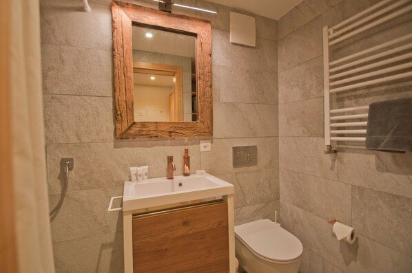A bathroom with a wooden-framed mirror, a white sink, a toilet, and a towel rack. - Studio Aosta (Zermatt)