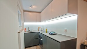 A modern kitchen with grey cabinets, a stainless steel countertop, and under-cabinet lighting. - Studio Aosta (Zermatt)