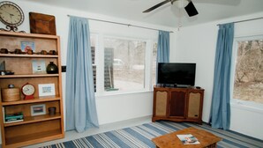Una sala de estar con televisor, una estantería de madera, una mesita y una ventana con cortinas.