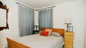 Un dormitorio con una cama individual, una mesita de noche con lámpara, un aparador y un espejo en la pared.