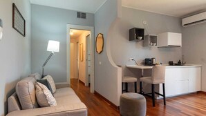 A compact living space with a sofa, ottoman, kitchenette, and a door leading to another room. - Pescara INN at Golf - Tiger Woods (Abruzzo)