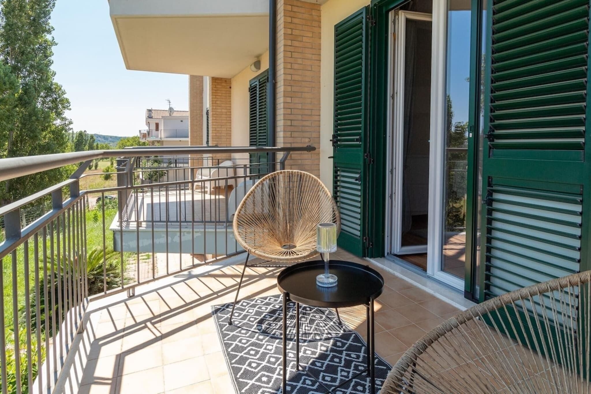 Un balcone con una sedia in vimini, un tavolino e un bicchiere d'acqua.