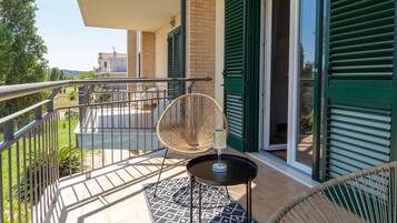 Un balcone con una sedia in vimini, un tavolino e un bicchiere d'acqua.