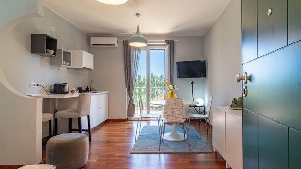 A modern kitchen with a built-in stove, a dining area with a round table and chairs, and a large window with curtains. - Pescara INN at Golf - Tiger Woods (Abruzzo)