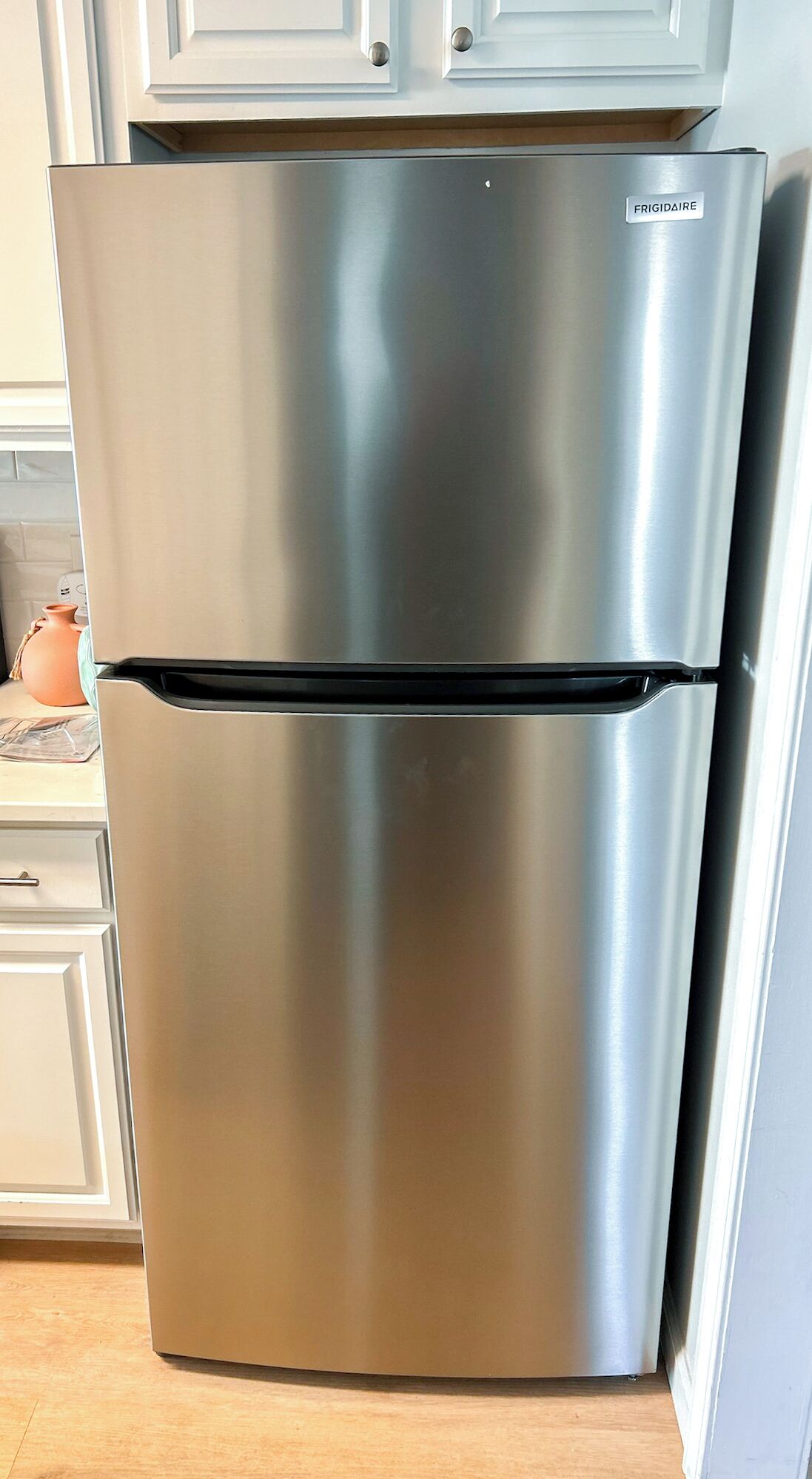Un réfrigérateur en acier inoxydable portant l’inscription « FRIGIDAIRE » se trouve dans une cuisine avec des armoires bleu clair et un comptoir en bois.