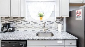 A kitchen with white cabinets, a granite countertop, a sink, a coffee maker, and a no-smoking sign. - Cozy Getaway with Pool and Putting Green - Unit 2 (Fort Lauderdale)