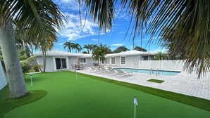 A golf course with a putting green, a pool, and a building in the background. - Cozy Getaway with Pool and Putting Green - Unit 2 (Fort Lauderdale)