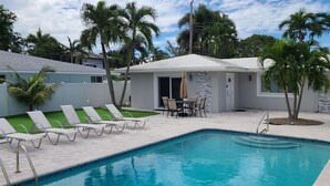 A swimming pool with lounge chairs, a small patio area, and a building with a stone facade. - Cozy Getaway with Pool and Putting Green - Unit 2 (Fort Lauderdale)