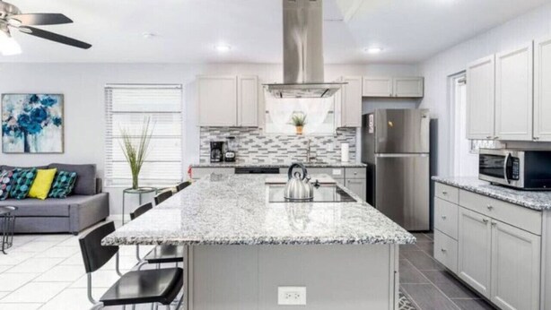 A modern kitchen with a central island, stainless steel appliances, and a grey sofa in the adjacent living area. - Cozy Getaway with Pool and Putting Green - Unit 2 (Fort Lauderdale)