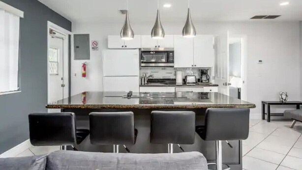A modern kitchen with white cabinets, a central island with bar stools, and pendant lighting.
