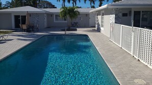 A swimming pool with a tiled deck, palm trees, and a white fence. - Cozy Getaway Studio with Pool and Putting Green 1A (Fort Lauderdale)