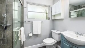 A modern bathroom with a glass shower enclosure, a toilet, and a vanity with a sink. - Cozy Getaway Studio with Pool and Putting Green 1A (Fort Lauderdale)