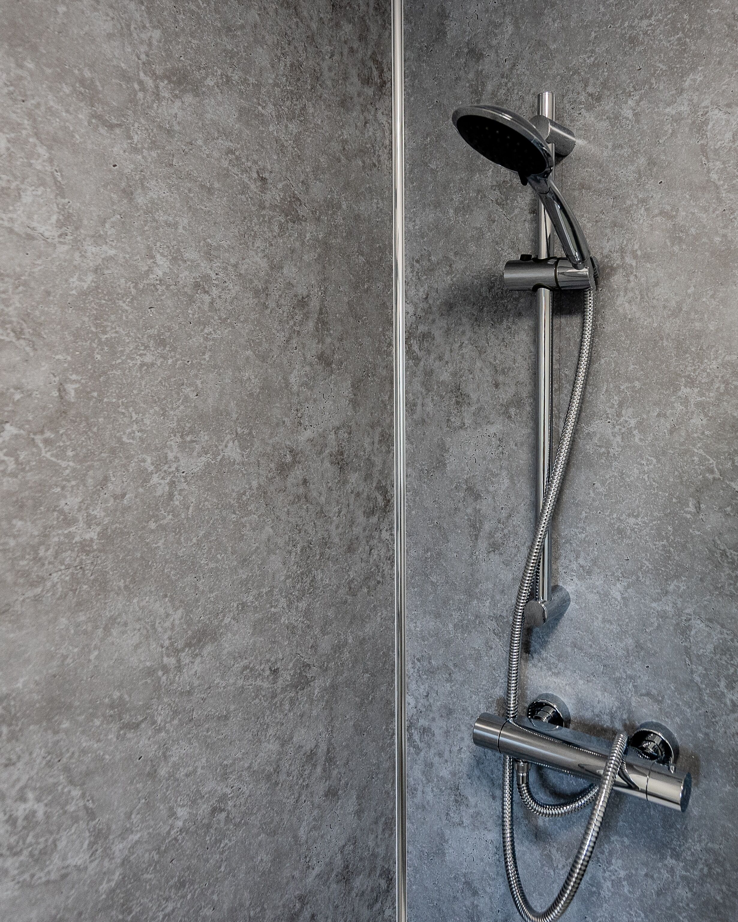 Een moderne douche met een handdouche en een vastzitende kraan aan de muur.