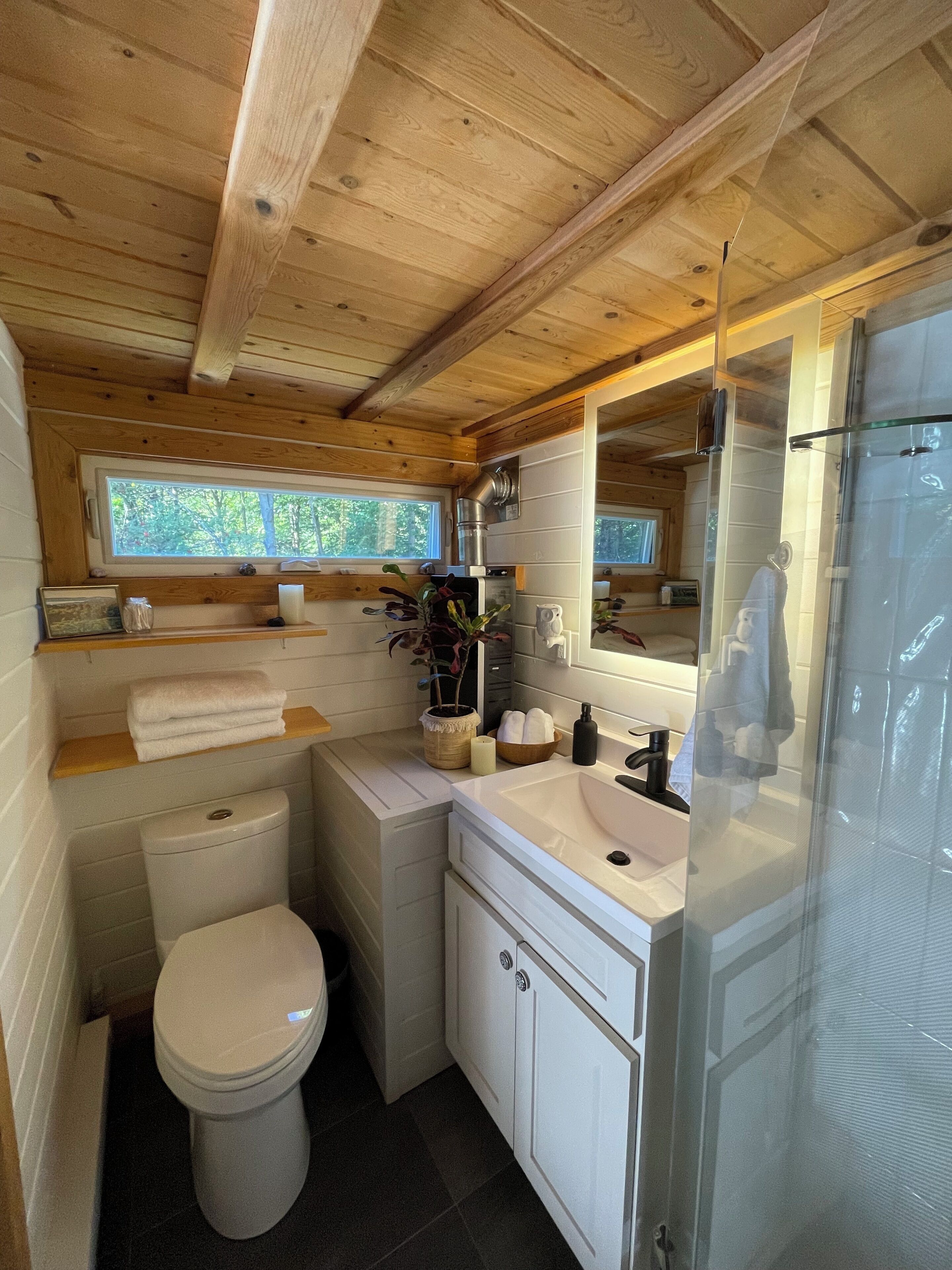 A compact wooden cabin bathroom with a toilet, sink, and shower.