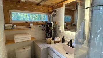 A compact wooden cabin bathroom with a toilet, sink, and shower.