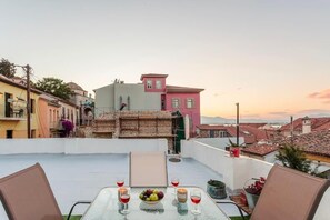 Une terrasse sur le toit, avec une table dressée pour le dîner, entourée d’immeubles aux toits recouverts de tuiles rouges, offrant une vue dégagée sur le paysage urbain.