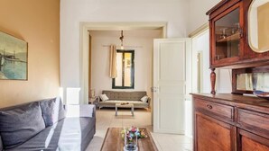 A living room with a sofa, a coffee table with decorative items, a wooden cabinet, and a painting on the wall. - Nafplia Guesthouse 1 (Nafplio)