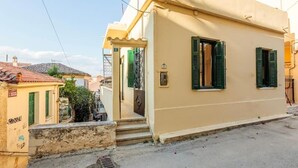 A beige building with green shutters, a visible door, and a small porch area. - Nafplia Guesthouse 1 (Nafplio)