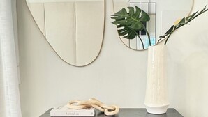 Un espejo con marco curvo, un florero con una planta y un libro titulado 'Minimalista' sobre una mesa de madera oscura.