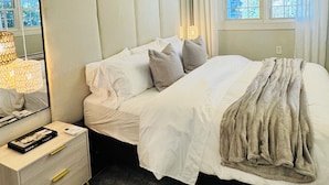 Un dormitorio con cama, mesita de noche, lámpara y ventana con cortinas.