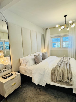 A bedroom with a bed, bedside table, lamp, and a window with curtains.