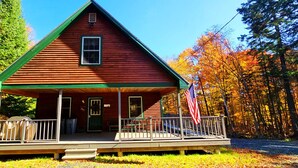 Une cabane rouge avec un porche, un drapeau et une forêt en arrière-plan.