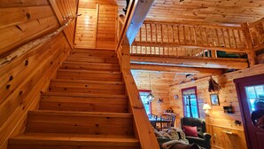 Un escalier en bois mène à une chambre mansardée avec vue sur l’extérieur.