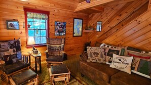 L’intérieur chaleureux d’un chalet avec des murs en bois, un fauteuil à bascule, un banc rembourré et une petite table avec une lampe.