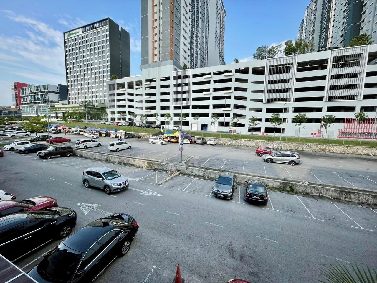 A parking lot with multiple cars, a multi-story parking garage, and high-rise buildings in the background.