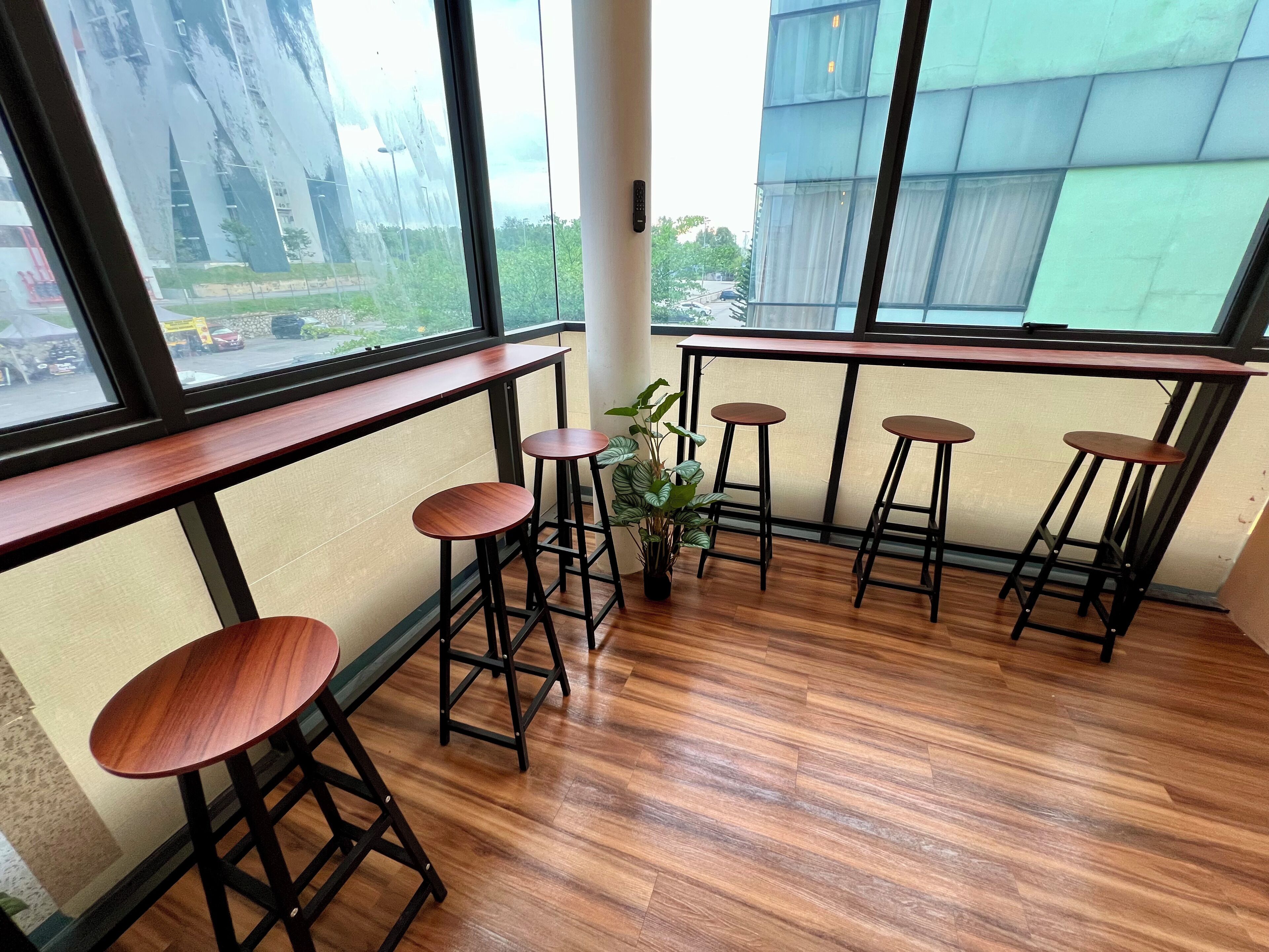 A corner of a room with wooden flooring, a window with a view of buildings and trees, and four wooden stools.
