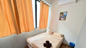 Un lit simple avec un matelas et des oreillers de couleur beige, un plancher en bois et des rideaux orange.