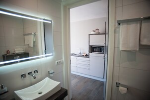 Un baño moderno con un espejo grande, lavamanos blanco y zona de ducha.