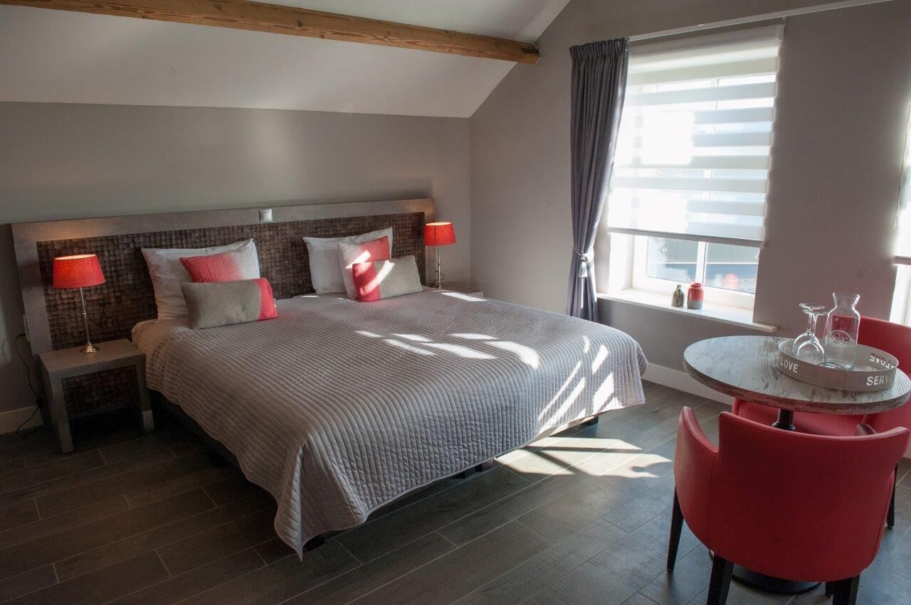 A bedroom with a large bed, two bedside tables with lamps, a small round table with a tray, and a window with curtains.